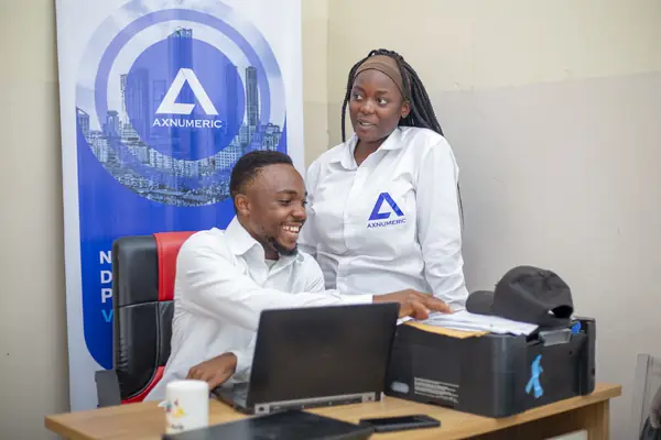 Deux collaborateurs souriants devant un ordinateur, la bannière AXNUMERIC derrière eux
